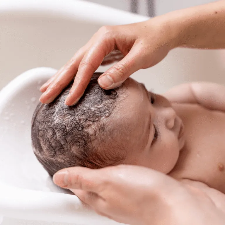 Parent’s hands washing a newborn’s hair during a bath