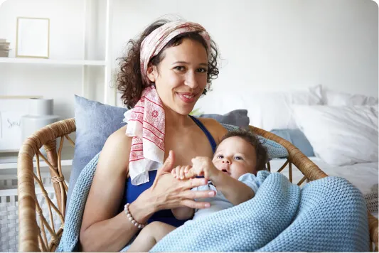 Smiling mother with a towel over her shoulder breastfeeding her baby in a wicker chair