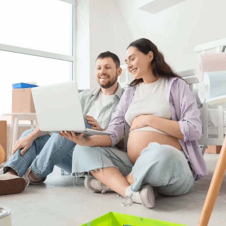 Expecting couple sitting on the floor at home, looking at a laptop together