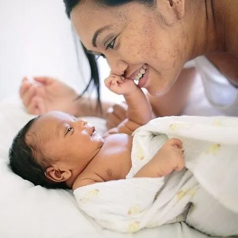 Mother smiling at her newborn lying on a soft blanket