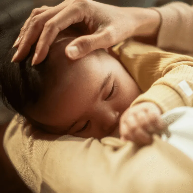 Parent’s hand gently stroking the head of a sleeping baby