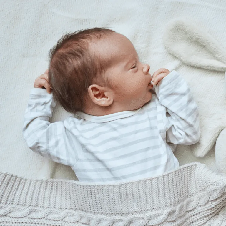 Newborn baby in a striped sleepsuit sleeping on its back on a soft blanket