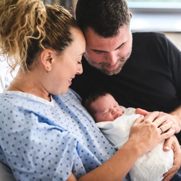New parents in a hospital bed smiling at their newborn baby