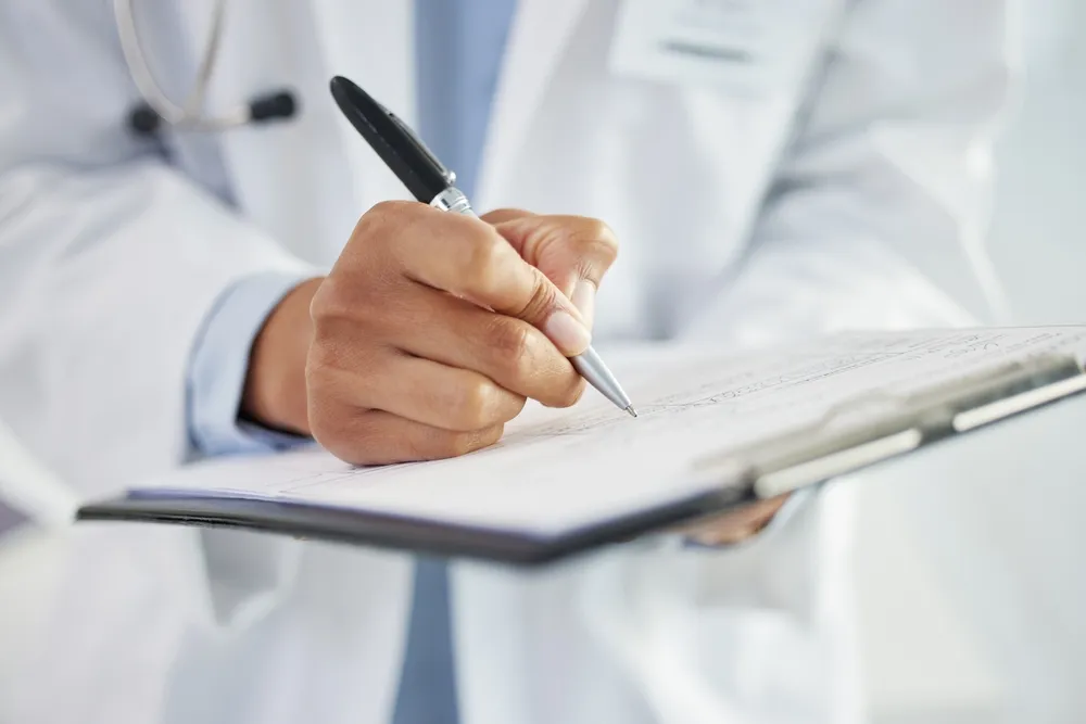 Provider in a white coat writing on a clipboard