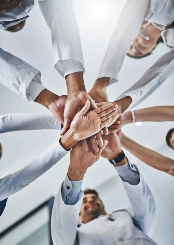 Healthcare team in white coats stacking their hands together in a circle, seen from below