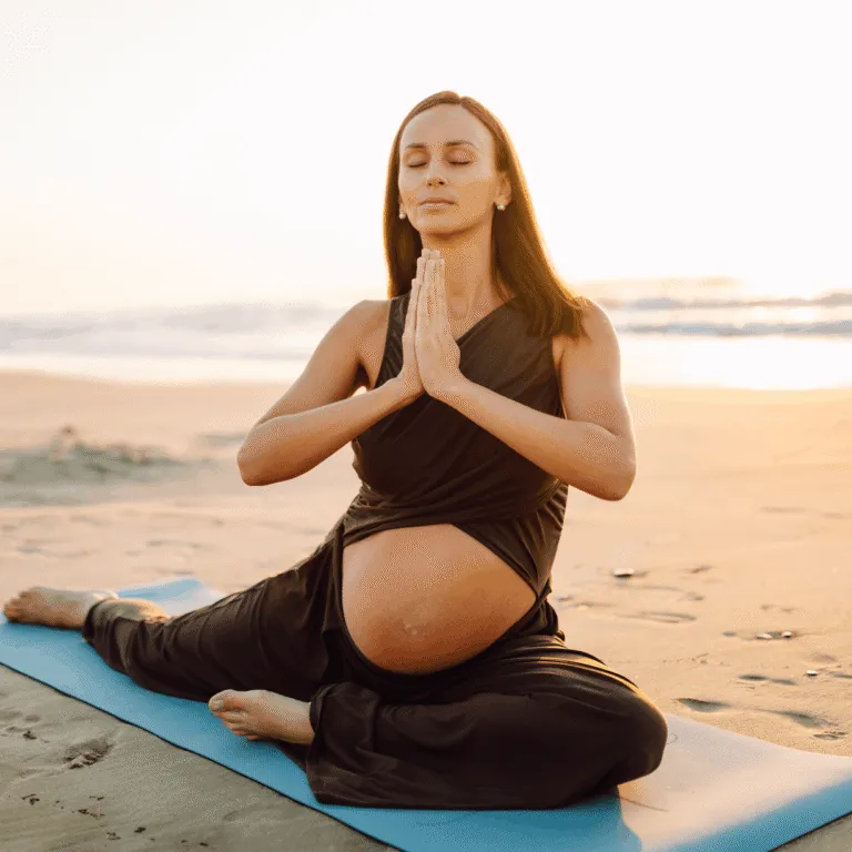 Pregnant woman meditating on a yoga mat on the beach at sunset